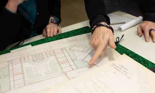 Vue sur les mains de 2 personnes qui consultent des documents présentés sur une table